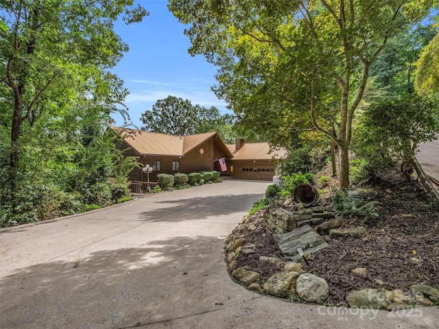 view of front of house featuring a garage, concrete driveway, metal roof, and a chimney