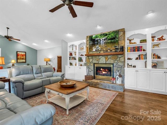 living room with a ceiling fan, lofted ceiling, wood finished floors, a stone fireplace, and built in shelves