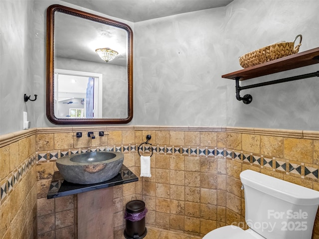 bathroom with toilet, a wainscoted wall, tile walls, and a sink