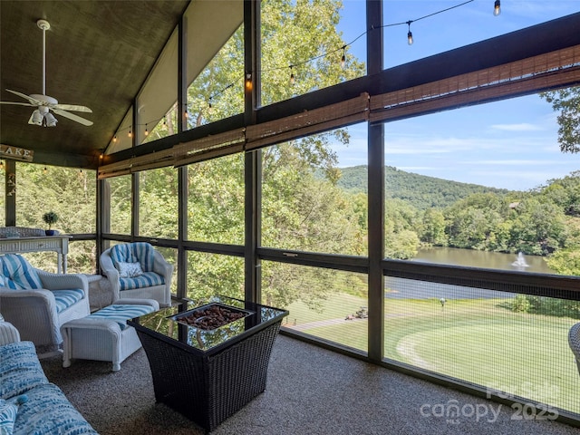 unfurnished sunroom with ceiling fan, vaulted ceiling, a water view, and a wooded view