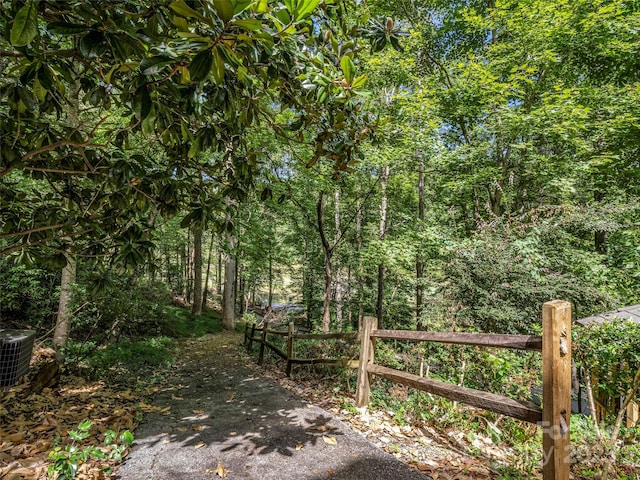 view of gate featuring fence, a view of trees, and central air condition unit