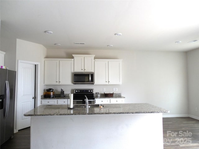 kitchen featuring a center island with sink, appliances with stainless steel finishes, dark hardwood / wood-style flooring, dark stone counters, and white cabinets