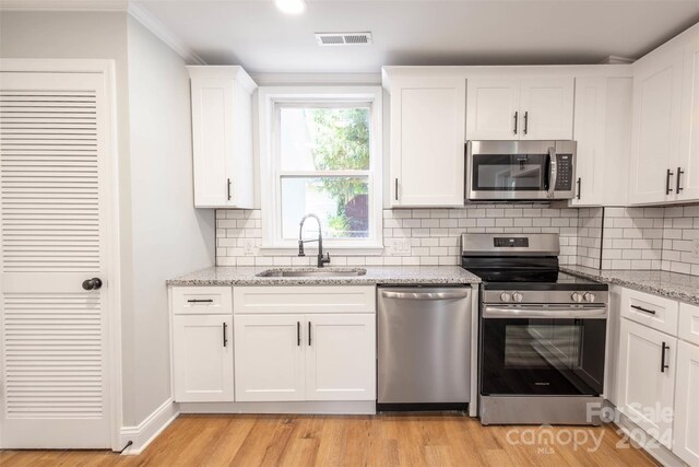 kitchen featuring stainless steel appliances, sink, light stone countertops, white cabinets, and light hardwood / wood-style floors