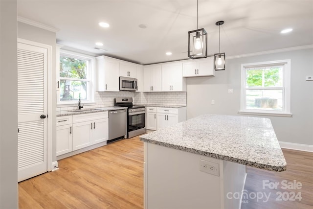 kitchen with white cabinetry, stainless steel appliances, a kitchen island, sink, and light stone countertops