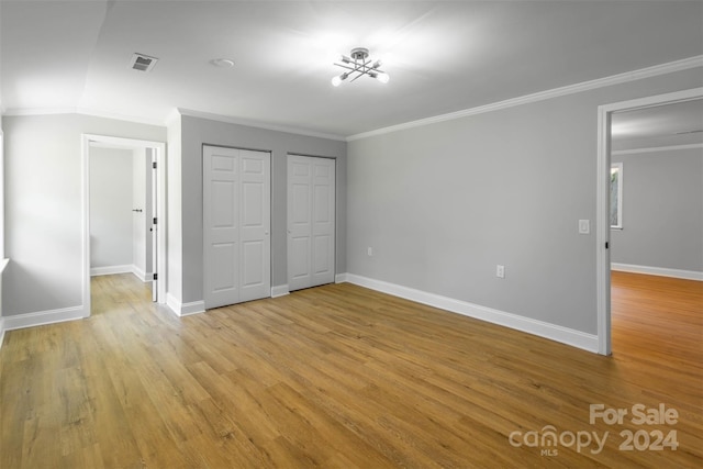 unfurnished bedroom with two closets, crown molding, and light hardwood / wood-style flooring