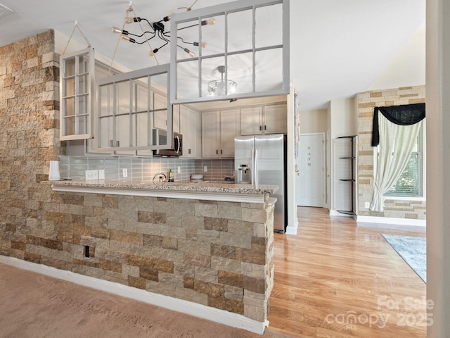 kitchen featuring appliances with stainless steel finishes, backsplash, light stone counters, kitchen peninsula, and light wood-type flooring