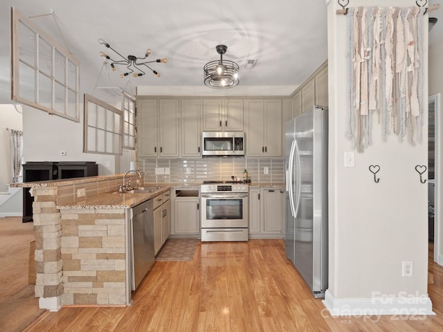 kitchen featuring pendant lighting, sink, stainless steel appliances, light stone countertops, and kitchen peninsula