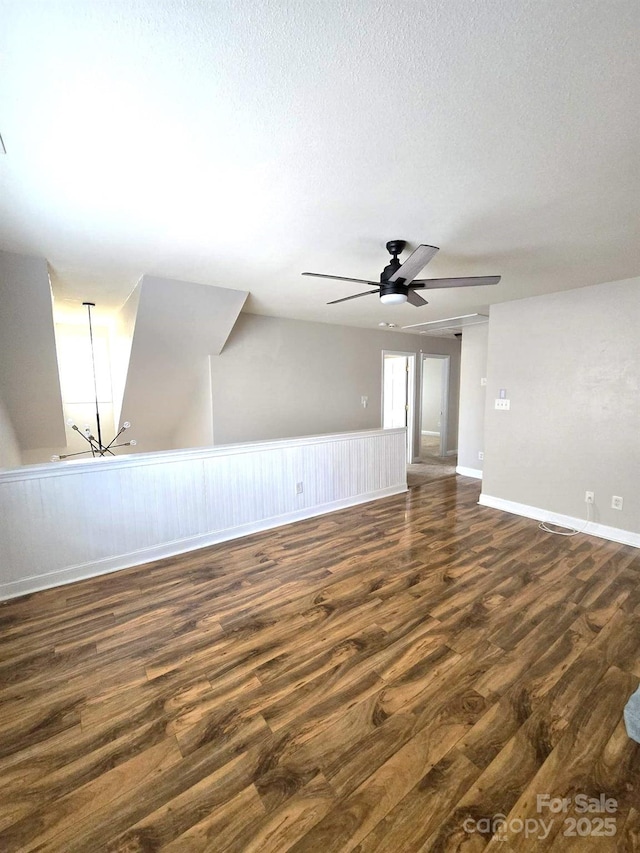 empty room with dark wood-type flooring, ceiling fan with notable chandelier, and a textured ceiling