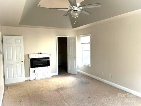 unfurnished bedroom featuring ceiling fan, a raised ceiling, vaulted ceiling, and light carpet