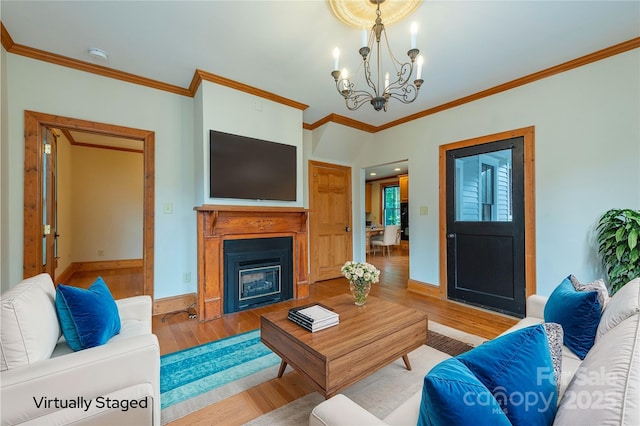 living area featuring a fireplace, light wood-style flooring, an inviting chandelier, ornamental molding, and baseboards