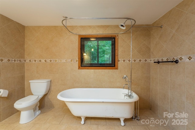 bathroom with toilet, a freestanding tub, tile patterned flooring, and tile walls