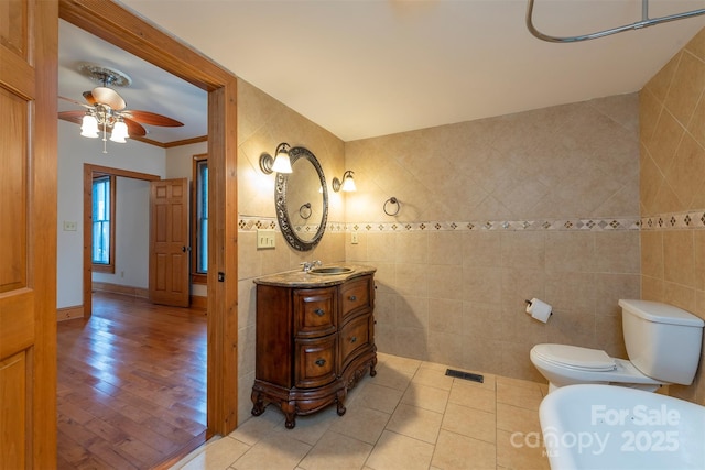 bathroom featuring crown molding, tile walls, toilet, vanity, and tile patterned floors