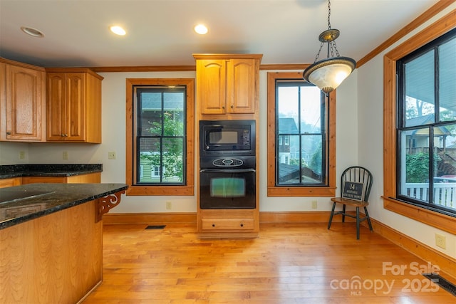 kitchen with dark stone counters, hanging light fixtures, crown molding, black appliances, and a wealth of natural light