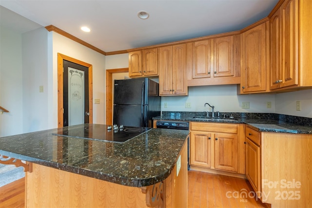 kitchen featuring a center island, light wood finished floors, a sink, dark stone countertops, and black appliances