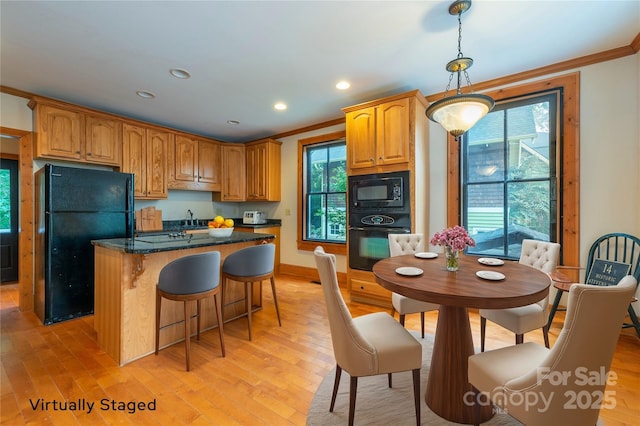 kitchen with light wood finished floors, black appliances, ornamental molding, and hanging light fixtures