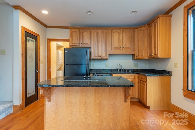 kitchen featuring freestanding refrigerator, a center island with sink, light wood finished floors, and dark stone countertops