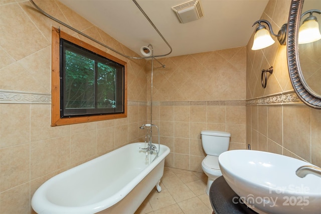 full bath featuring visible vents, toilet, a sink, a freestanding tub, and tile walls