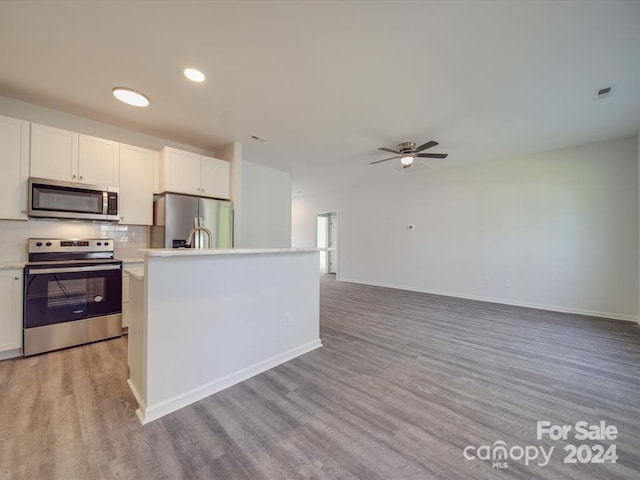 kitchen featuring stainless steel appliances, wood-type flooring, ceiling fan, a center island with sink, and white cabinets