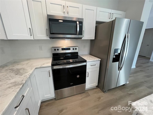 kitchen with stainless steel appliances, tasteful backsplash, white cabinets, and light hardwood / wood-style floors