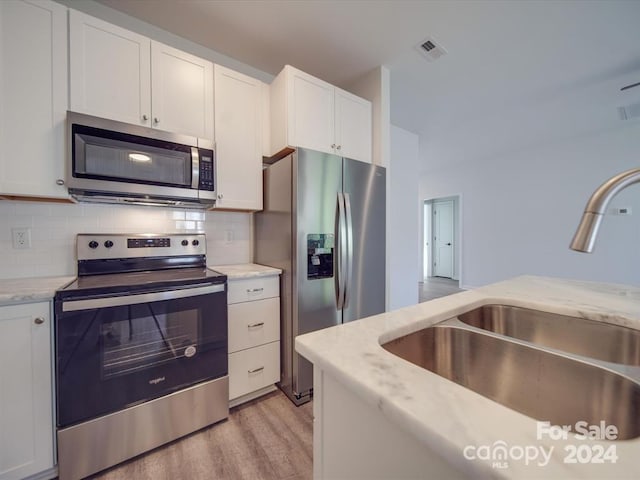 kitchen with white cabinetry, light hardwood / wood-style flooring, backsplash, sink, and appliances with stainless steel finishes