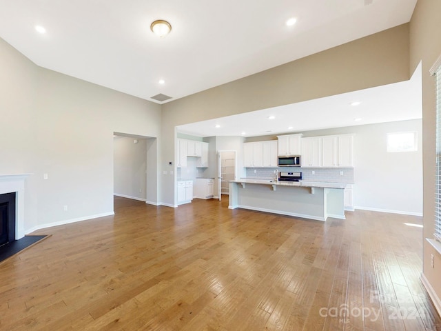 unfurnished living room with visible vents, baseboards, light wood-type flooring, a fireplace, and recessed lighting