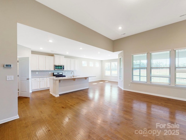 kitchen with gas range oven, stainless steel microwave, backsplash, light wood-style floors, and open floor plan