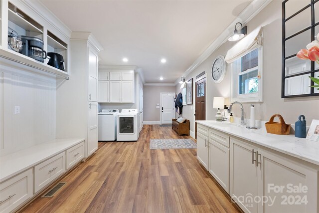 kitchen featuring crown molding, light hardwood / wood-style floors, white cabinetry, sink, and washing machine and clothes dryer