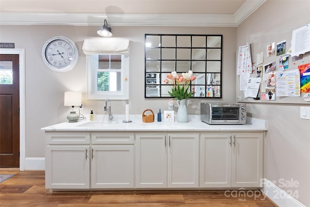 kitchen featuring crown molding, sink, light stone countertops, white cabinets, and light hardwood / wood-style floors