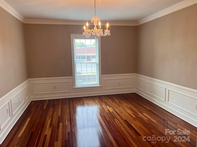 empty room featuring a chandelier, a wainscoted wall, dark wood finished floors, and ornamental molding