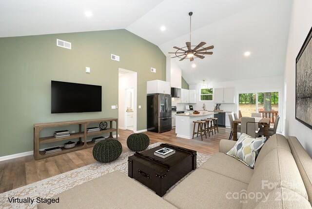 living room with ceiling fan, light wood-type flooring, sink, and high vaulted ceiling