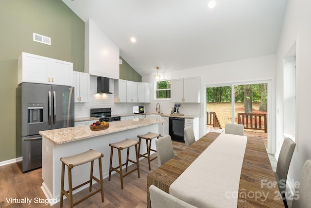 kitchen with wall chimney range hood, a breakfast bar, a center island, black appliances, and white cabinets