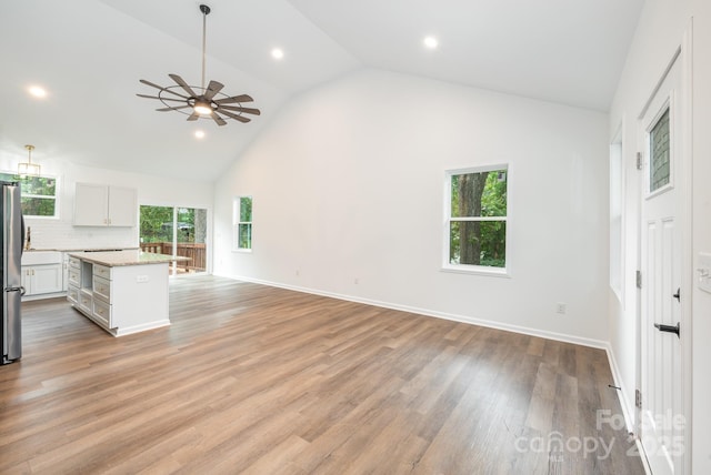 kitchen with a kitchen island, stainless steel refrigerator, white cabinets, hanging light fixtures, and light stone counters