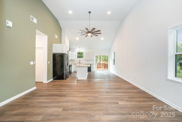 unfurnished living room with ceiling fan, high vaulted ceiling, sink, and light wood-type flooring