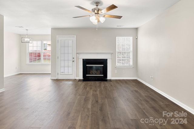 unfurnished living room with ceiling fan with notable chandelier and dark hardwood / wood-style floors