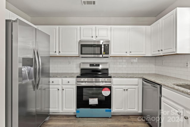 kitchen featuring tasteful backsplash, white cabinets, light stone countertops, dark hardwood / wood-style flooring, and stainless steel appliances