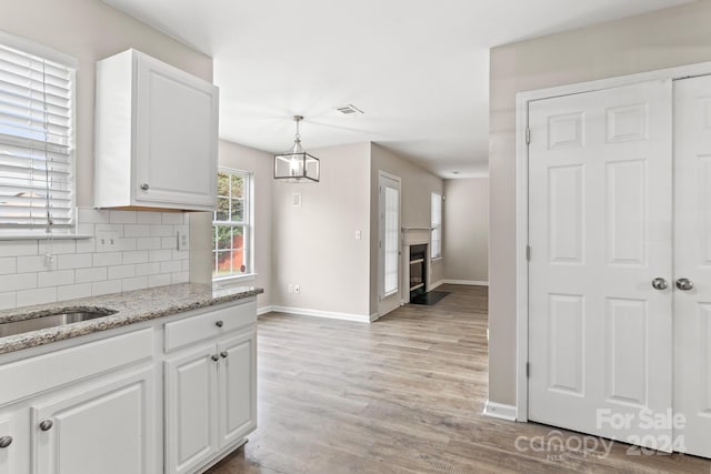 kitchen featuring light stone counters, pendant lighting, tasteful backsplash, white cabinetry, and light hardwood / wood-style floors