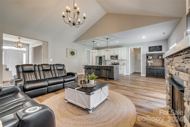 living room with a fireplace, vaulted ceiling, an inviting chandelier, and light hardwood / wood-style floors