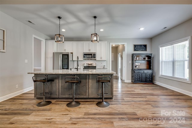 kitchen with a breakfast bar area, an island with sink, stainless steel appliances, light stone counters, and white cabinets