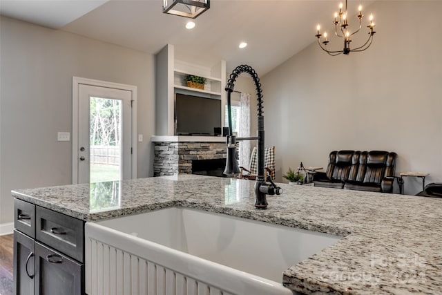 kitchen featuring hardwood / wood-style floors, light stone countertops, a chandelier, sink, and a stone fireplace