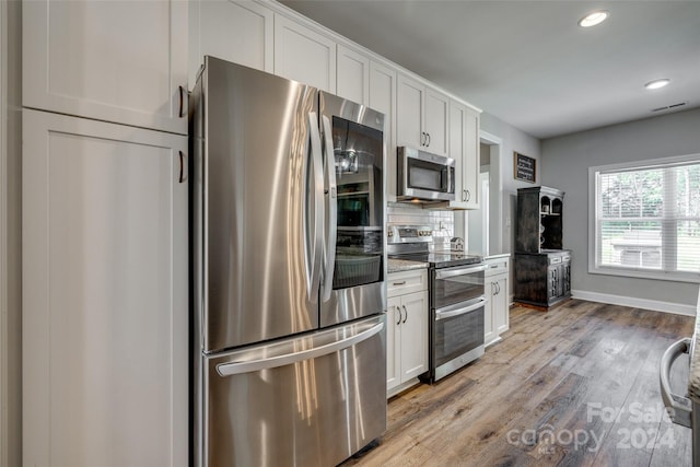 kitchen featuring backsplash, light wood-type flooring, light stone counters, stainless steel appliances, and white cabinetry