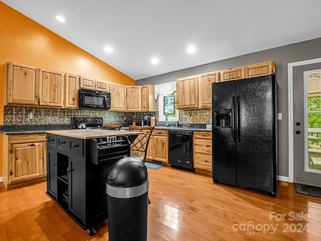 kitchen with light wood-type flooring, black appliances, a center island, vaulted ceiling, and light brown cabinets