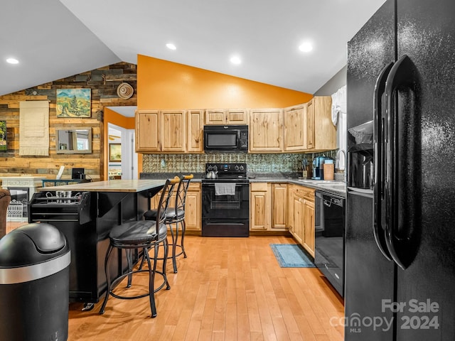 kitchen with light wood-type flooring, a kitchen breakfast bar, black appliances, light brown cabinetry, and lofted ceiling