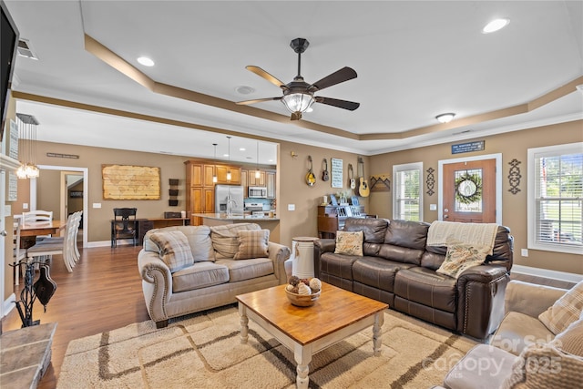 living room featuring ornamental molding, light hardwood / wood-style floors, a raised ceiling, and ceiling fan