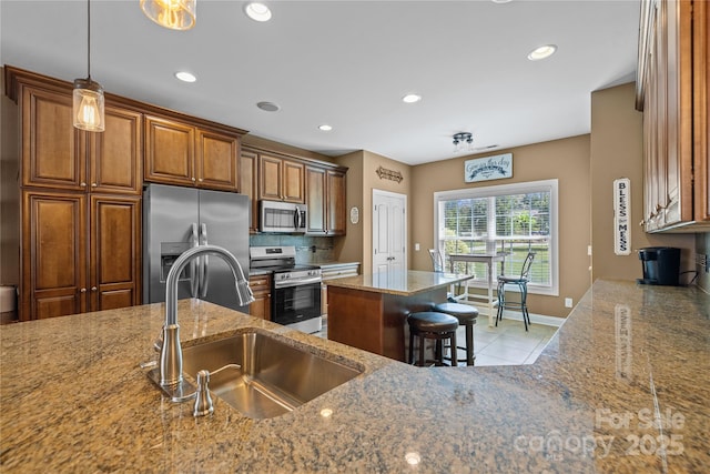 kitchen with a kitchen island, appliances with stainless steel finishes, sink, a kitchen bar, and light stone countertops