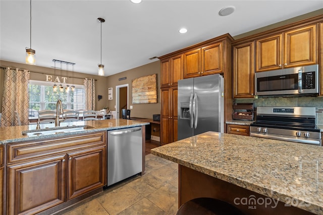 kitchen featuring stainless steel appliances, light stone countertops, sink, and pendant lighting