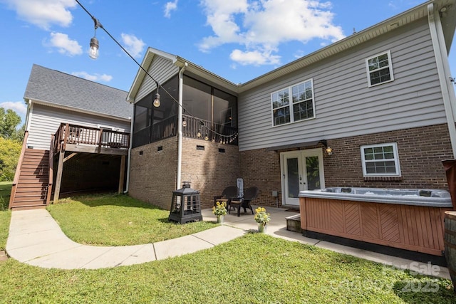 rear view of property with a fire pit, a lawn, a patio area, a sunroom, and a hot tub