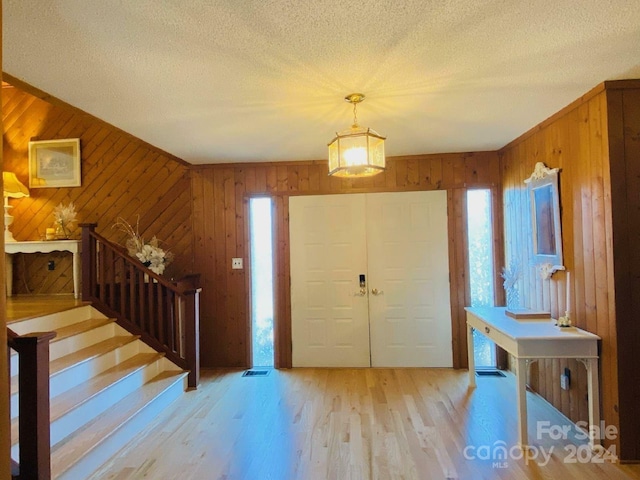 foyer entrance featuring a textured ceiling, light wood-type flooring, and wooden walls