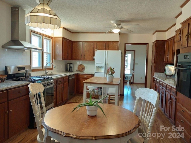 kitchen featuring stainless steel appliances, sink, wall chimney range hood, dark hardwood / wood-style floors, and ceiling fan