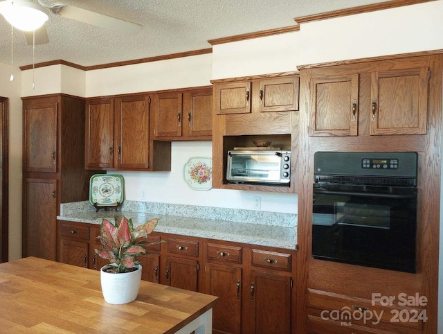 kitchen with a textured ceiling, butcher block countertops, crown molding, ceiling fan, and black oven