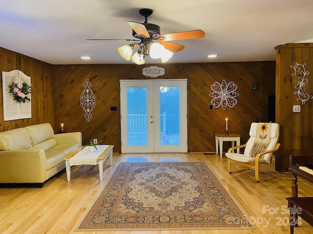 living room with ceiling fan, wood walls, light wood-type flooring, and french doors